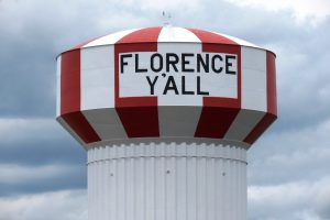 Red and white striped water tower with a sign reading 'FLORENCE Y'ALL' under a cloudy sky.