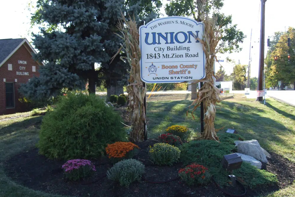 Sign for Union City Building with corn-stalk decorations and a colorful flower bed in front of a small brick building.
