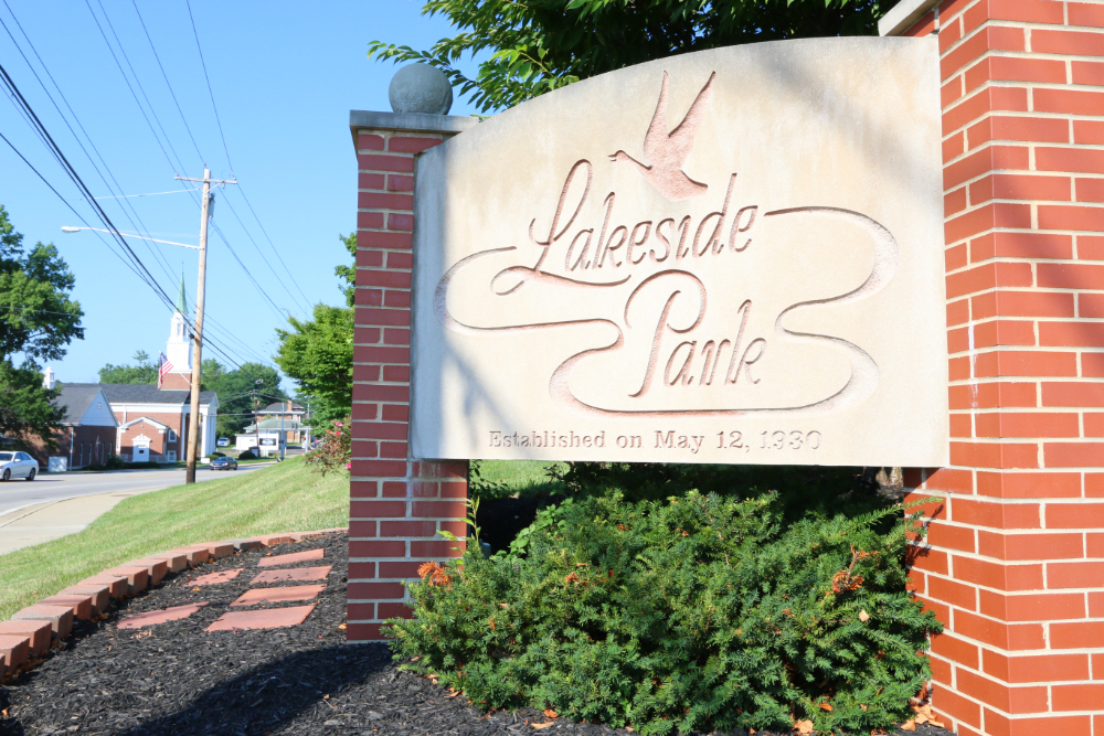 Lakeside Park entrance sign on brick pillars with a curved light-colored plaque and greenery around, established May 12, 1930.