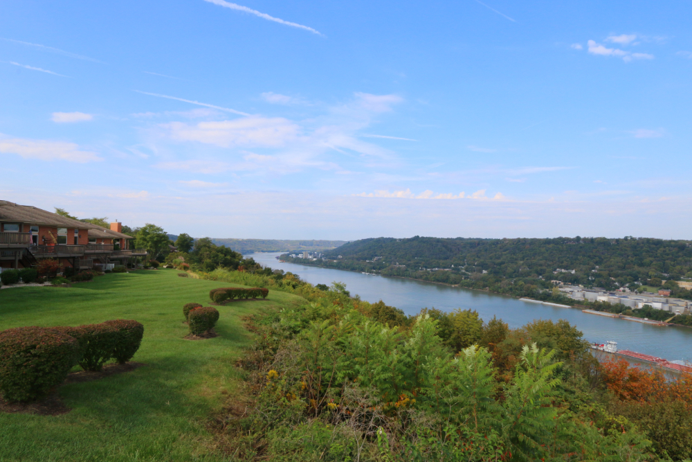 Lawn with trimmed hedges on a hillside overlooking a wide river and distant town beyond.